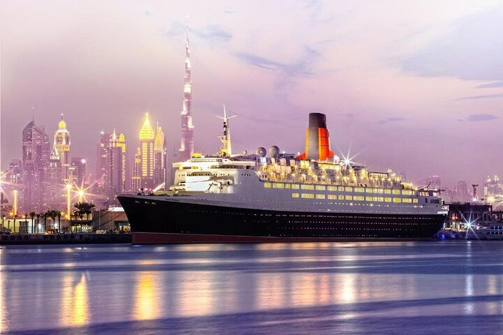 Experience a unique blend of history and indulgence aboard the Queen Elizabeth 2 enjoying delightful teas and treats while exploring the legacy of this iconic ship against Dubai's stunning skyline.